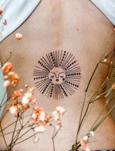 a woman's back with an intricate sun tattoo on her left side and flowers in the foreground