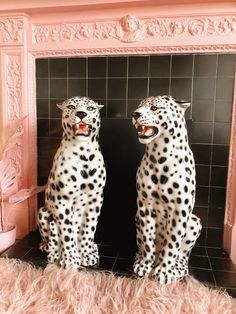 two white and black leopard statues sitting in front of a pink fireplace