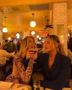 two beautiful women sitting at a table with wine glasses in their hands and plates on the table