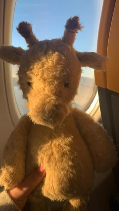 a stuffed animal sitting on top of an airplane window sill next to a person's hand