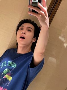 a young man taking a selfie with his cell phone in the air while wearing a blue shirt