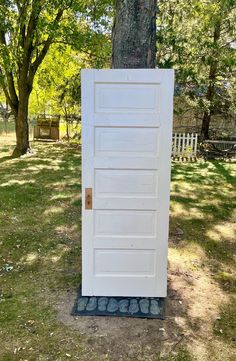 a white door sitting in the grass next to a tree