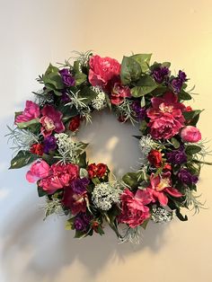 a pink and purple flower wreath hanging on the side of a wall with greenery