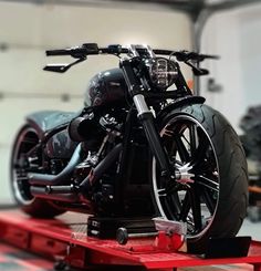 a black motorcycle is sitting on a red dolly in a garage with other motorcycles behind it