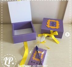 a purple box with a yellow ribbon and a notepad in it next to a small gift bag