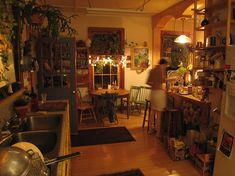 a woman standing in a kitchen next to a sink and window with plants on the shelves