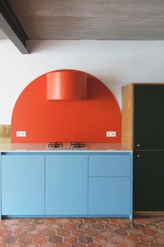 a kitchen with blue cabinets and an orange wall behind the stove top, along with brick flooring