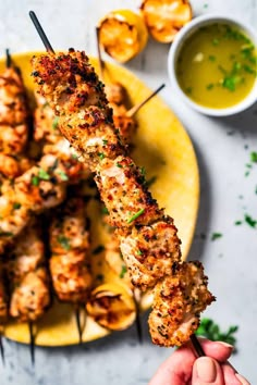 a person holding a skewer of chicken on a plate with dipping sauces