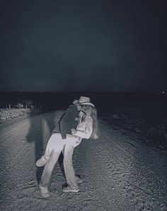 two people standing in the middle of an empty road at night, one person is holding a baby