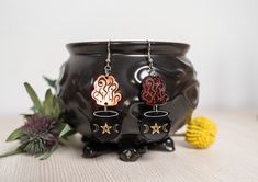 These cute witch mystical cauldron earrings are laser cut and engraved on Midnight Prism Iridescent acrylic. The hooks and stud posts are made from surgical stainless steel wire and are great for sensitive ears. FEATURES * Durable laser cut acrylic. * Laser engraved design that won't wear away. * Lightweight and comfortable to wear all day. * Durable surgical stainless steel wire hooks. MATERIAL * Laser cut and engraved acrylic. * Hypoallergenic surgical stainless steel. * Other hook options are Creepy Earrings, Trailer Decor, The Black Cauldron, Gothic Earrings, Holiday Earring, Laser Cut Acrylic, Skull Earrings, Halloween Earrings, Accessories Jewelry Earrings