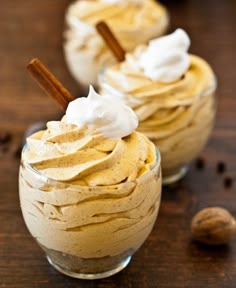 two desserts with whipped cream and cinnamon sticks in glass bowls on a wooden table