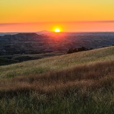 the sun is setting over a grassy hill