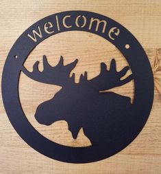 a welcome sign with a moose's head in the center on a wooden surface