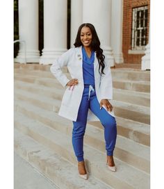 a woman standing on steps in front of a building wearing blue pants and a white jacket