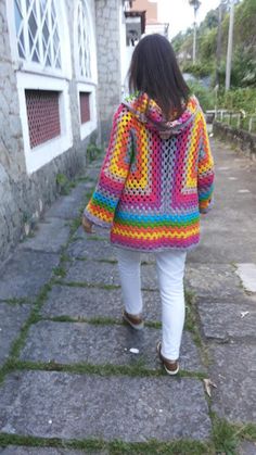 a woman is walking down the street wearing a multicolored jacket and white pants