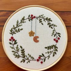 the embroidery hoop is decorated with red berries and green leaves, along with a gold leaf charm