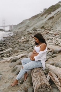 a pregnant woman sitting on a log at the beach