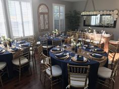 a dining room set up with blue and white table cloths, gold chargers and place settings