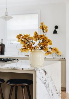 a vase with yellow flowers sitting on top of a kitchen counter next to two stools