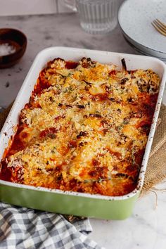 a green casserole dish filled with lasagna and cheese on a table