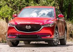 the front end of a red mazda cx - 5 parked on a gravel road