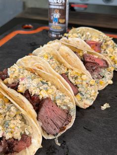 four steak tacos are lined up on a counter with a bottle of alcohol in the background