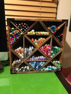 a wooden box filled with lots of crayons on top of a green table