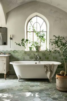 a white bath tub sitting under a window next to a potted plant in a bathroom