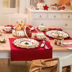 the table is set for christmas dinner with red and white plates, silverware, and other holiday decorations