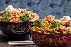 two bowls filled with noodles, broccoli and carrots