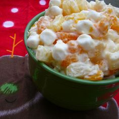 a green bowl filled with fruit salad on top of a red table cloth next to an orange towel