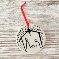 a ceramic ornament hanging from a red ribbon on a white wooden surface with black and white designs