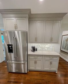 a stainless steel refrigerator in a kitchen with white cabinets and wood flooring is shown