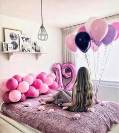 a woman sitting on top of a bed with pink and purple balloons in the air