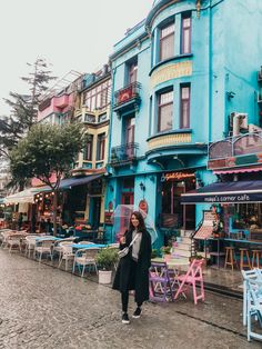 a woman standing in front of a blue building with tables and chairs on the sidewalk