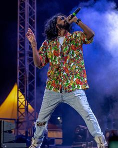 a man with long hair on stage singing into a microphone and holding his hands up in the air