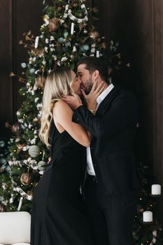 a man and woman kissing in front of a christmas tree