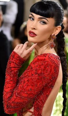 a woman in a red dress with braids on her head and hand near her face