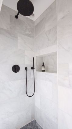 the shower head is mounted to the wall in this white tiled bathroom with black fixtures