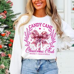 a woman standing next to a christmas tree wearing a white shirt with pink bows on it