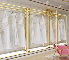 a room filled with lots of white dresses hanging on gold racks next to a pink chair