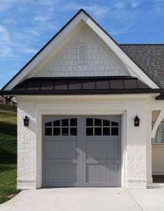 a white house with a black roof and two garage doors