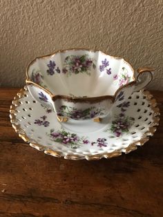 an antique teacup and saucer with flowers on them sitting on a wooden table