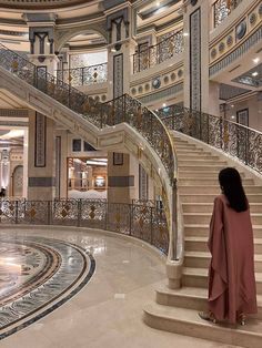 a woman standing in front of a spiral stair case with marble floors and railings