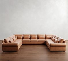 a large tan leather sectional sofa sitting on top of a hard wood floor next to a white wall