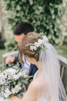 a bride and groom sitting on a bench with flowers in their hair looking at each other