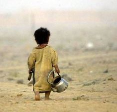 a little boy walking across a dirt field carrying a bucket and a water can in his hand