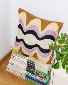 a pile of books sitting on top of a wooden table next to a plant and a pillow