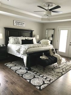 a bedroom with a large bed, black and white rugs, wooden flooring and ceiling fan