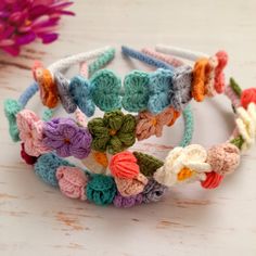 several crocheted flower headbands sitting on top of a white table next to a pink flower